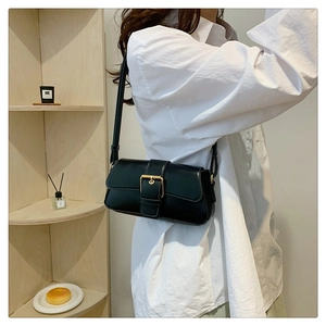 Close-up of black glossy leather shoulder bag with a gold buckle and slim strap