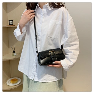 Close-up of a black crossbody bag with golden buckle on a model in a cozy room