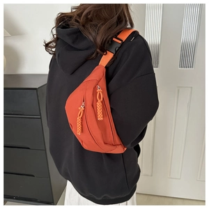 Détail du sac bandoulière en nylon orange avec tirettes tressées et sangle sur le mannequin