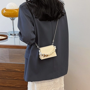 Mini sac bandoulière en cuir crème avec chaîne en perles et cœurs dorés sur le mannequin