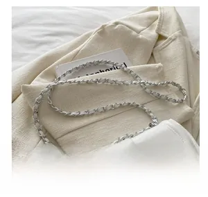 Detail of white leather saddle bag showing metal chain and leather braided shoulder strap