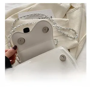 Close-up of white mini flap bag with silver magnetic snap buckle and chain strap