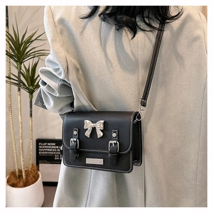 Detail of black crossbody bag with silver bow buckle and white contrast stitching