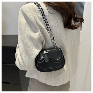 Detail view of a black saddle crossbody bag with silver chain strap and metal trim