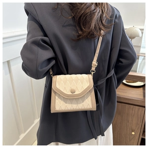 Petit sac beige matelassé porté à l'épaule sur un blazer gris pour un look moderne