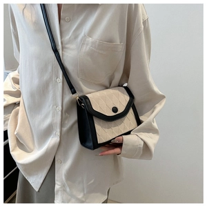 Gros plan du sac bandoulière beige matelassé avec bord noir porté par le mannequin