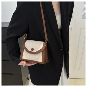 Détail du sac bandoulière matelassé avec bordure marron et boucle ronde décorative