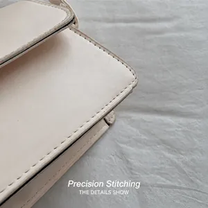 Détail macro des coutures de qualité sur le sac carré minimaliste blanc crème bandoulière