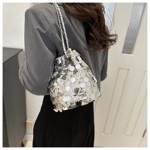 Detail view of a silver sequined bucket bag with a metal chain shoulder strap on a model
