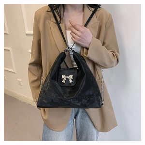 Detail of black velvet handbag featuring silver bow buckle and dual chain strap design