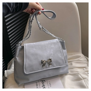 Detail of grey-blue shoulder bag featuring a metal bow buckle and chain strap