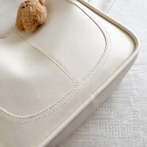 Detailansicht der cremefarbenen Tasche mit feinen Nähten und braunem Plüschbär-Anhänger