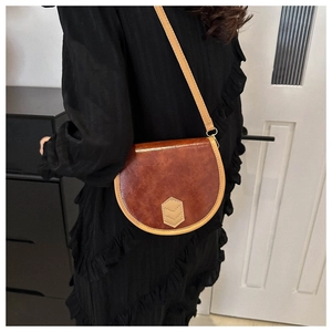 Detailed view of a vintage reddish-brown saddle bag worn crossbody on a black dress