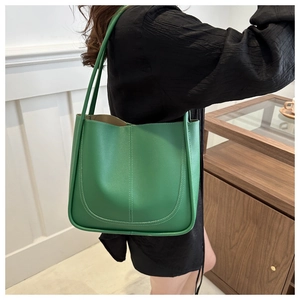 Dettaglio della borsa tote in pelle verde con cuciture a U indossata da una modella
