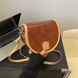 Vintage brown saddle shoulder bag with contrast trim on a dark desk with laptop