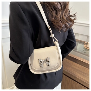 Detailed view of cream-white saddle bag featuring a stylish silver metal bow buckle