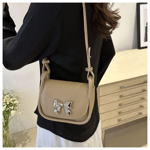 Close-up of beige saddle bag featuring a silver bow buckle and adjustable strap