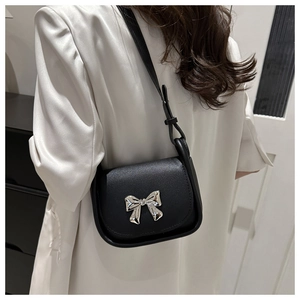 Close-up of black crossbody bag with silver bow buckle and fine textured leather