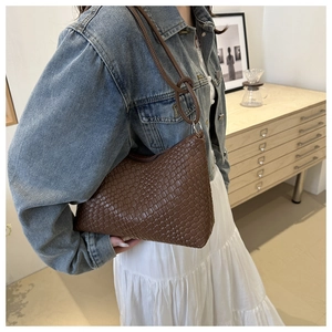 Dettaglio borsa a spalla intrecciata marrone scuro su modella con giacca di jeans