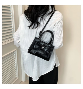 Detail of a black glossy crossbody bag featuring a large bow and silver heart clasp