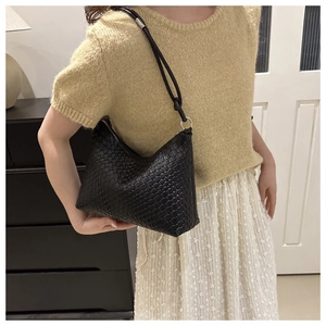 Dettaglio della borsa hobo intrecciata nera e tracolla indossata da una modella in interni