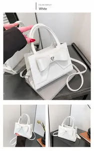 Detailed view of white patent leather handbag with bow and heart metal buckle accent