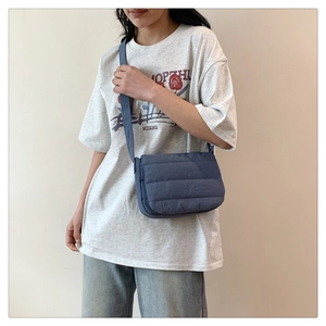 Detalle de un bolso bandolera acolchado azul llevado por una modelo en un entorno minimal