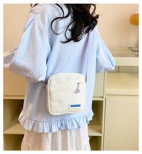 Détail d'un sac bandoulière en toile blanche avec sangle violette et patch logo