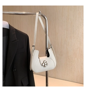 Détail d'un sac demi-lune blanc avec fermoir floral en métal sur un présentoir