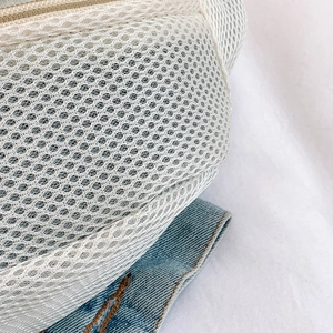 Detail shot of breathable off-white mesh fabric and metal zipper on a casual chest bag