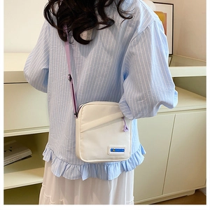 Détail d'un sac à bandoulière en toile blanche avec sangle violette et étiquette fashion