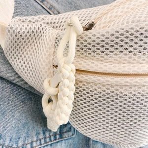 Close-up of mesh fabric with woven rope zipper detail on white crossbody chest bag