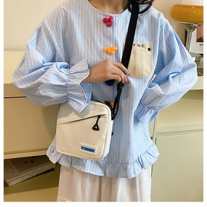 Sac bandoulière en toile blanche avec étiquette Fashion porté sur une chemise bleue