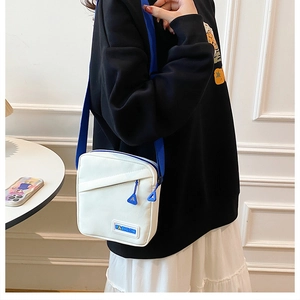 Détail du sac bandoulière en toile blanche avec zip bleu et étiquette mode sur mannequin