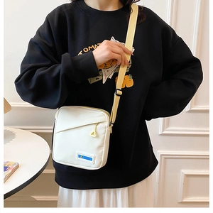 Détail du sac à bandoulière en toile blanche avec sangle jaune et étiquette de mode devant