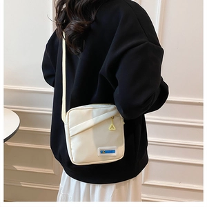 Détail du sac bandoulière en toile crème avec zip jaune et écusson tendance fashion