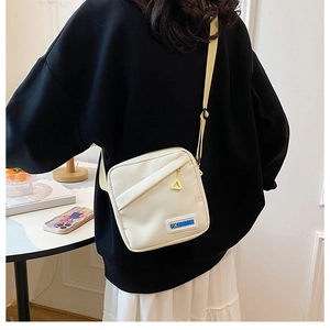 Détail d'un sac bandoulière en toile beige minimaliste avec étiquette mode et zip métal