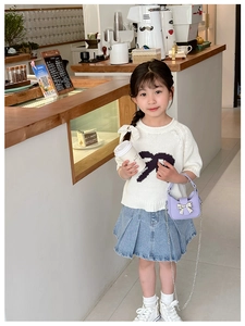 Detail of a purple mini chain bag with bow clasp on a child in a denim pleated skirt