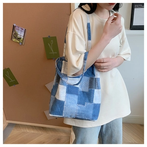 Detail of color-block denim tote bag showing blue patchwork textures and wide shoulder strap