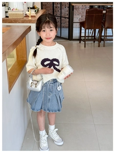 Detail of a child's cream knit sweater with bow and pleated denim skirt with silver bag