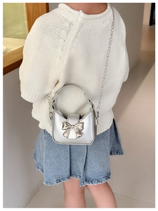 Detail of silver kids handbag with metal bow and chain strap on a white knit sweater