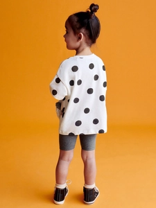 Girl's white polka dot long sleeve top and grey cycling shorts set on orange background