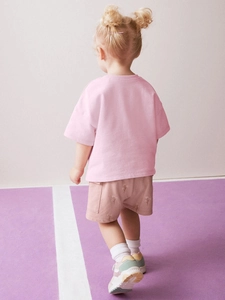 Vista posteriore del set estivo da bambina con maglietta rosa in cotone e pantaloncini