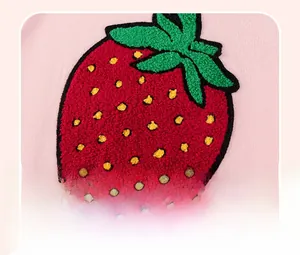 Détail macro d'une broderie de fraise en tissu bouclété sur un pull rose pour filles