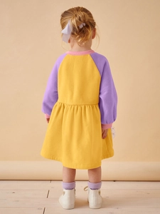 Mädchen Langarm-Patchwork-Kleid mit gelbem Rock und lila Ärmeln auf beigem Hintergrund