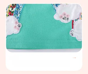 Detail of mint green cotton dress hem with white cloud applique and floral embroidery