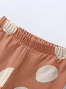 Elastic waistband detail of girls knit trousers with large polka dots in rust brown color