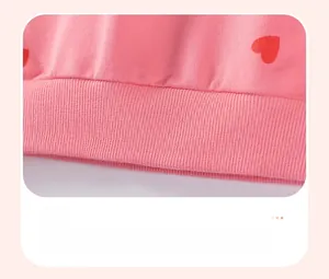 Detailed close-up of pink knit sweatshirt featuring red heart prints and ribbed hem