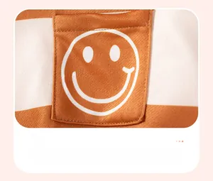 Détail du sweat rayé orange pour garçon avec une poche ornée d'un visage souriant