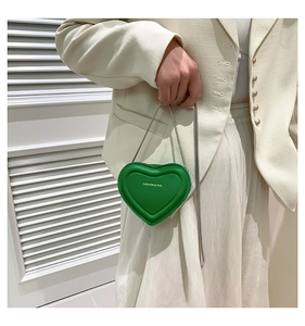 Detail of green heart-shaped mini leather bag with silver chain and stitched edges